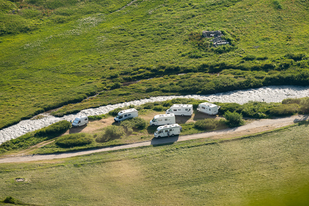 Six motorhomes parked close together at a small camping area next to stream.