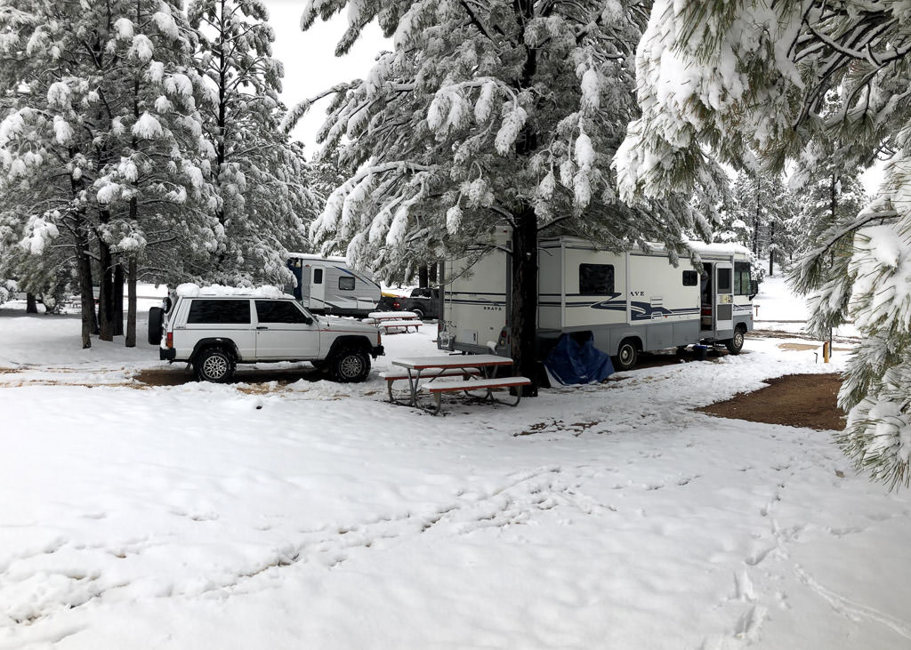Winnebago Brave parked in campsite with snow covered trees and snow on the ground.